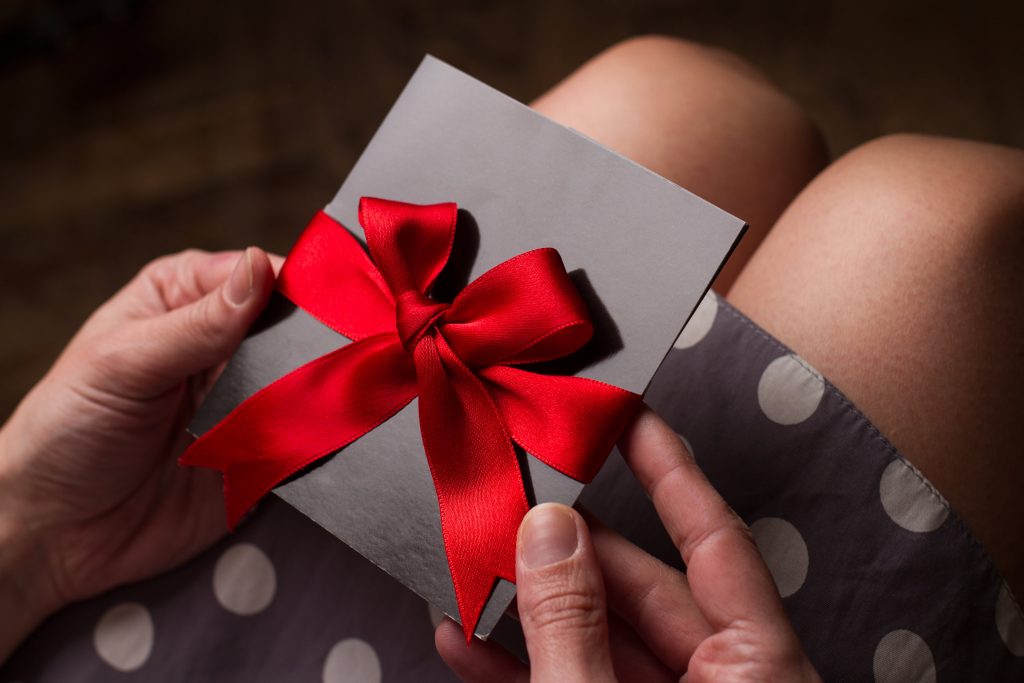 Close up of the hands of a woman with polka dress holding a black card with red ribbon above knees to illustrate Festive Vouchers and Rewards | Element